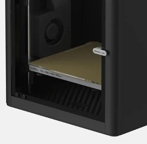 Interior de uma impressora 3D fechada visto pela porta de vidro, com a mesa de impressão e a ventoinha do fundo