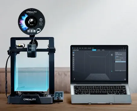 Impressora 3D Creality Ender 3 V3 SE ao lado de um notebook com o programa de fatiamento aberto na tela